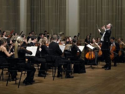 Orchestra performing in a grand concert hall with conductor leading.