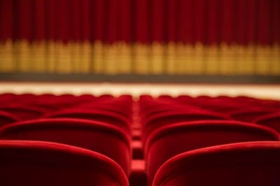 Empty red seats in a theater with closed curtains in the background.