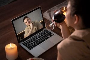 Person pouring wine during a virtual meeting on laptop.