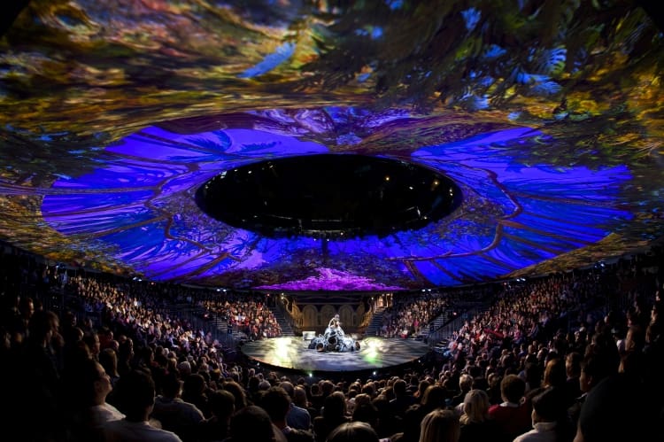 A grand concert with vibrant lighting and a large audience in a circular arena.