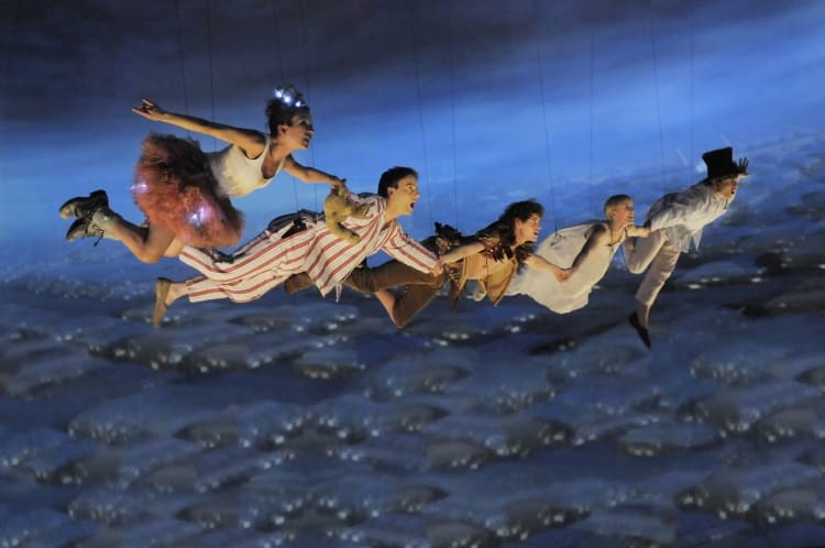 Children fly joyfully above a rocky shore under a twilight sky.