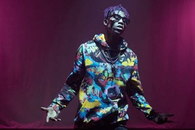 Person wearing colorful hoodie with expressive pose under purple lighting.