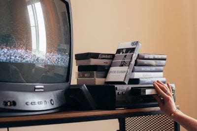Retro TV and VHS tapes on a shelf with a hand reaching out.