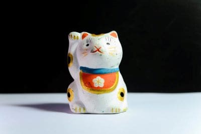 A small ceramic lucky cat figurine with a raised paw on a white surface.