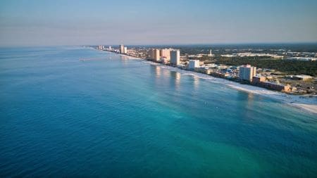 Aerial view of a coastal city with clear blue water and buildings along the shoreline.