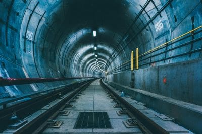 Empty underground tunnel with railway tracks and dim lighting.