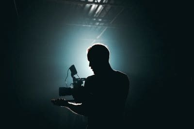 Silhouette of a man holding a laptop in a dark, foggy room with dramatic lighting.