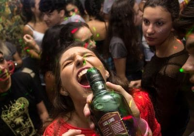 A woman drinking from a bottle at a crowded party.