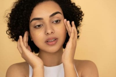 Young woman gently touching her face against beige background.