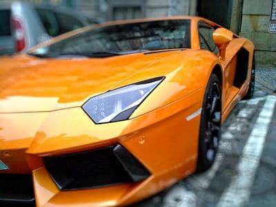 Close-up of an orange sports car's front headlight and wheel.