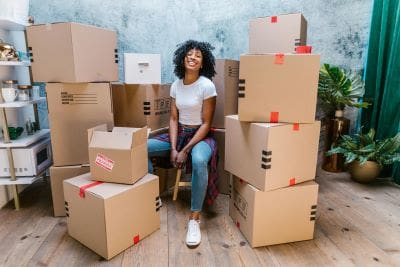 Young woman sitting among stacked moving boxes, smiling.