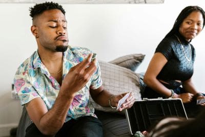 Man sitting on couch counting money with woman in background.