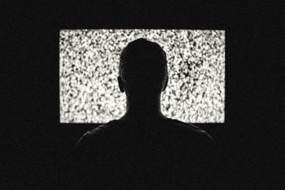 Silhouette of a person facing a static-filled TV screen in a dark room.