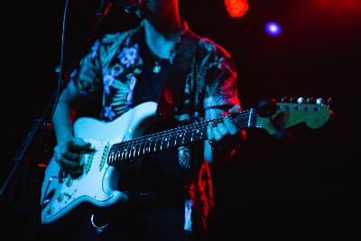 A musician playing electric guitar on stage under colorful lights.