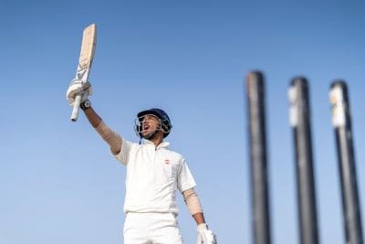 Cricket player celebrating with bat raised high on the field.