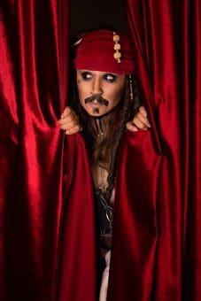 Person dressed as Jack Sparrow peeking through red curtains.