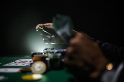 A person shuffling poker chips on a green table under dim light.