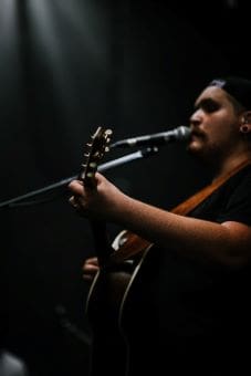 Musician passionately singing and playing guitar on stage in dim lighting.