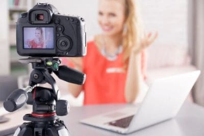 A woman recording a video with a camera and laptop in front of her.