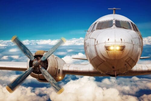 A vintage propeller airplane flying above the clouds under a clear sky.