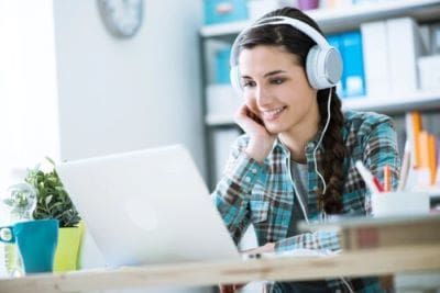 Young woman with headphones smiling at laptop screen.