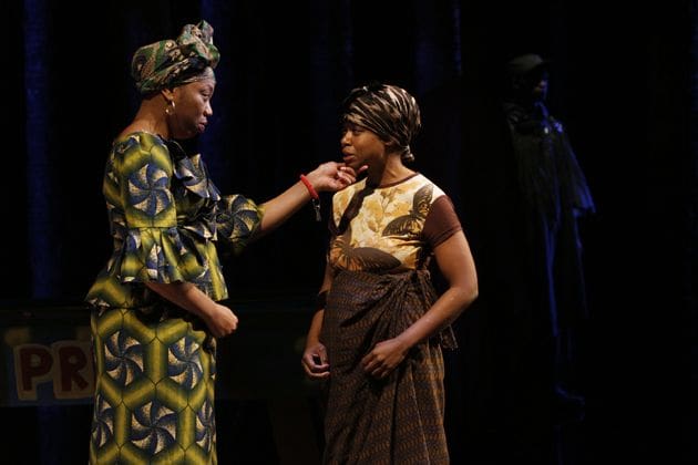 Two actors in traditional African attire perform a scene on stage.