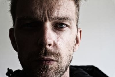 Close-up of a serious man with a beard and intense gaze.