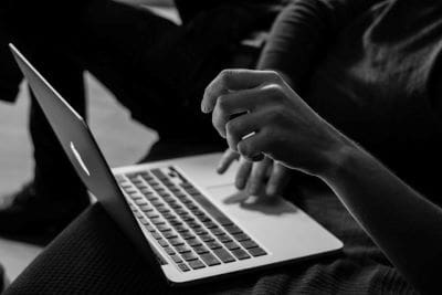 Close-up of hands typing on a laptop keyboard in black and white.
