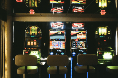 Empty chairs face a row of colorful slot machines in a casino.