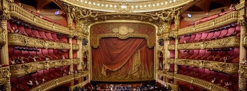 Ornate theater stage with a grand red curtain and intricate gold detailing.