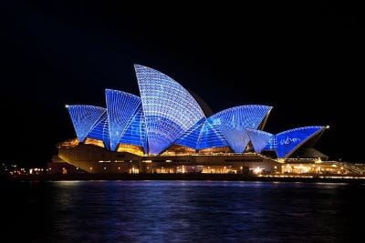 Sydney Opera House illuminated with blue lights at night.