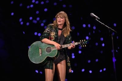 Female musician playing a teal guitar on stage with starry lights.