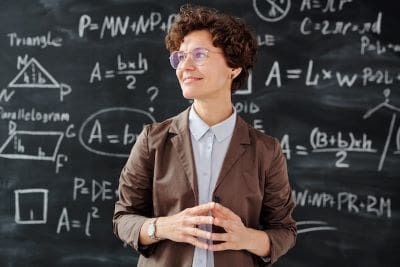 Young teacher standing confidently in front of a math-filled blackboard.