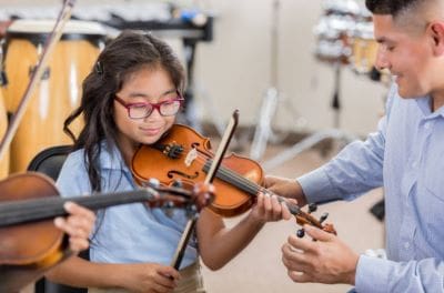 A young girl learning violin with guidance in a music classroom.