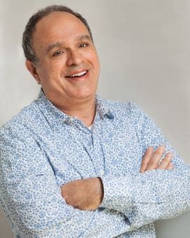 Smiling man in a patterned shirt with arms crossed.