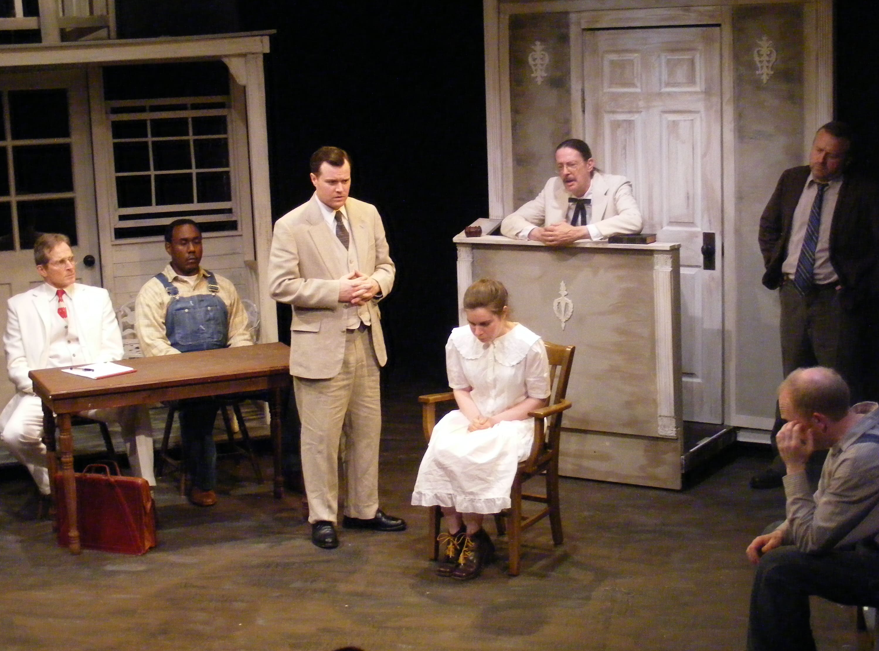 Actors perform a dramatic scene on stage with vintage props and costumes.