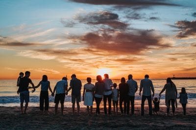 Group of people holding hands at sunset on the beach.