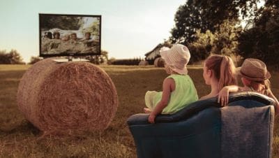 Child watches wildlife on TV outdoors near hay bale.