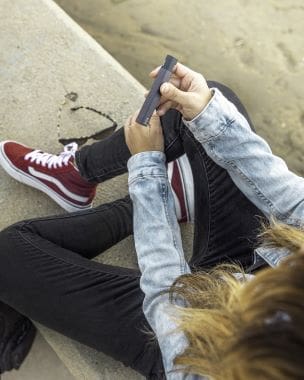 Person wearing red sneakers and a denim jacket using a smartphone.