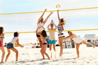 People playing beach volleyball on a sunny day near the ocean.