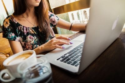 Woman typing on laptop in cozy cafe with coffee nearby.