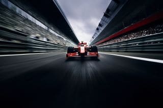 A red Formula 1 car speeding between grandstands on a race track.