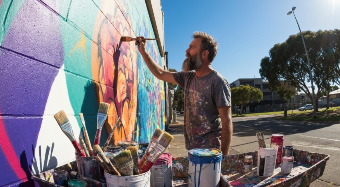 Artist painting a colorful mural outdoors under clear sky.