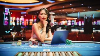 Confident woman at a casino poker table with chips and laptop.
