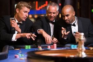 Three men in tuxedos playing poker at a casino table.
