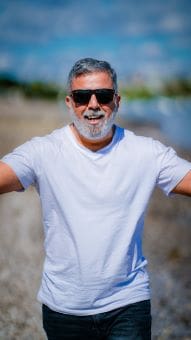 Smiling man in sunglasses wearing a white t-shirt outdoors.
