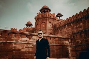 Man in sunglasses stands in front of an ancient red sandstone fort.