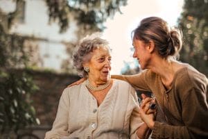 Two women share a warm moment outdoors, one elderly and one younger.