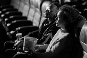 Two people enjoying a movie with popcorn and drinks in a theater.