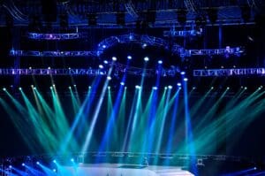Bright blue and green stage lights beam down in a dark venue.